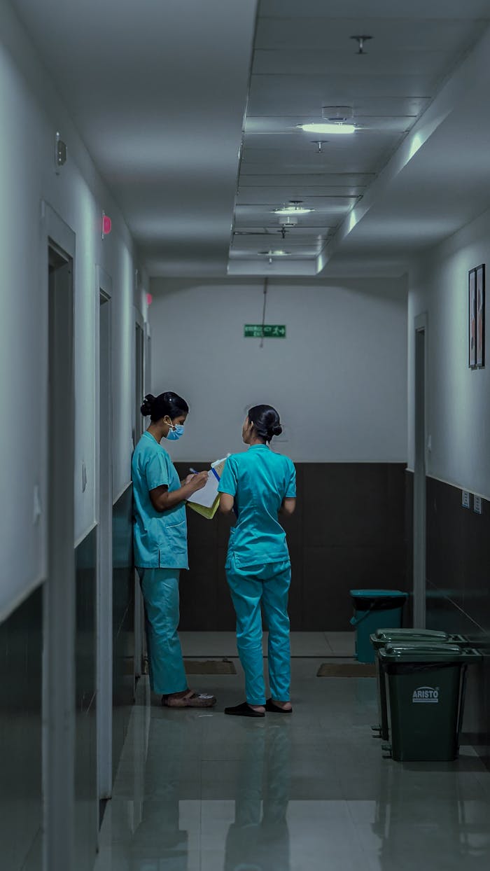 Two nurses in scrubs discussing patient notes in a hospital corridor.